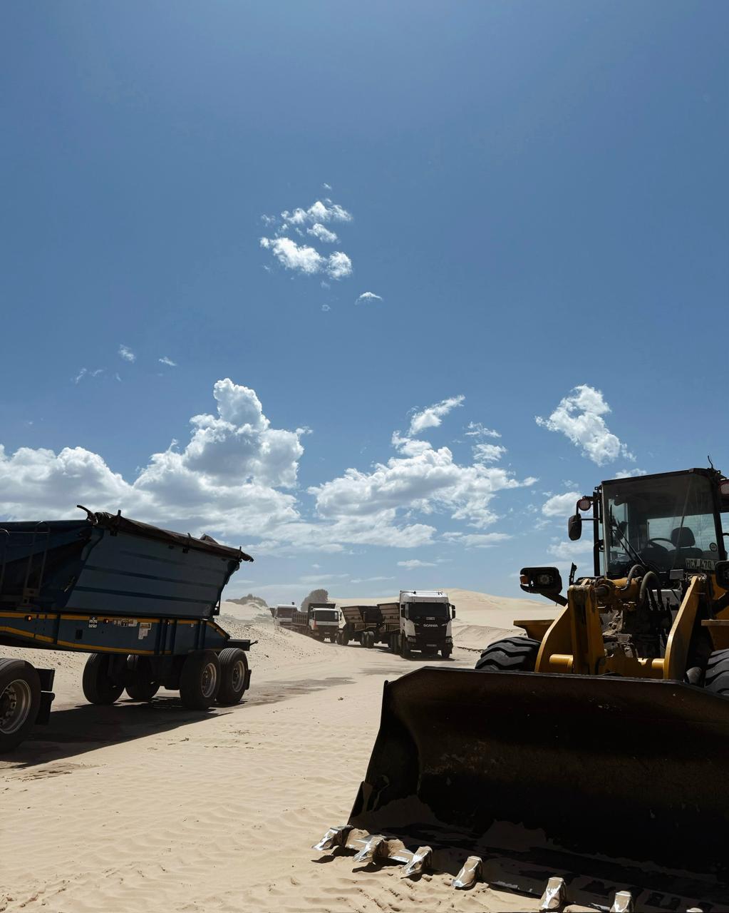 Wide shot of CWG Logistics convoy with Komatsu loader foreground on sand site